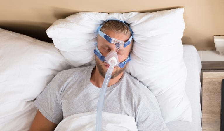 Nukkuva mies käyttää uniapnean hoitoon tarkoitettua CPAP-laitetta