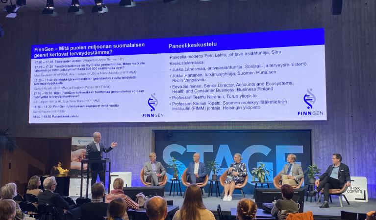 Paneldebatten börjar, på scenen finns moderatorn och fem panelister, i bakgrunden finns Tiedekulman STAGE-text och programbild.