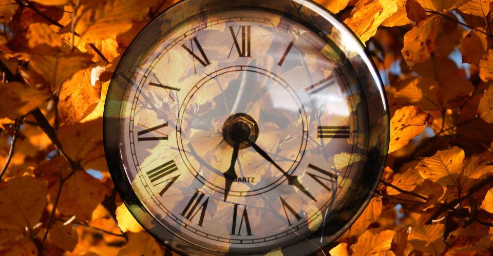 En gammaldags klocka med höstlöv i bakgrunden.