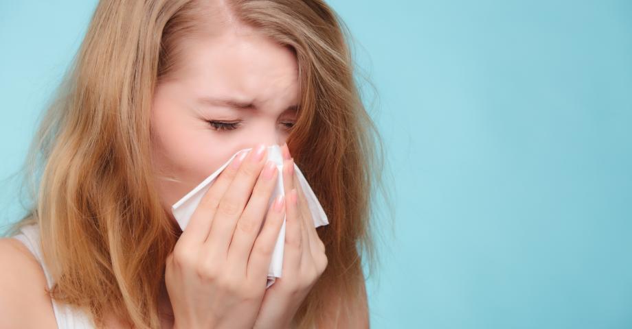 A sick girl sneezing in a tissue. 