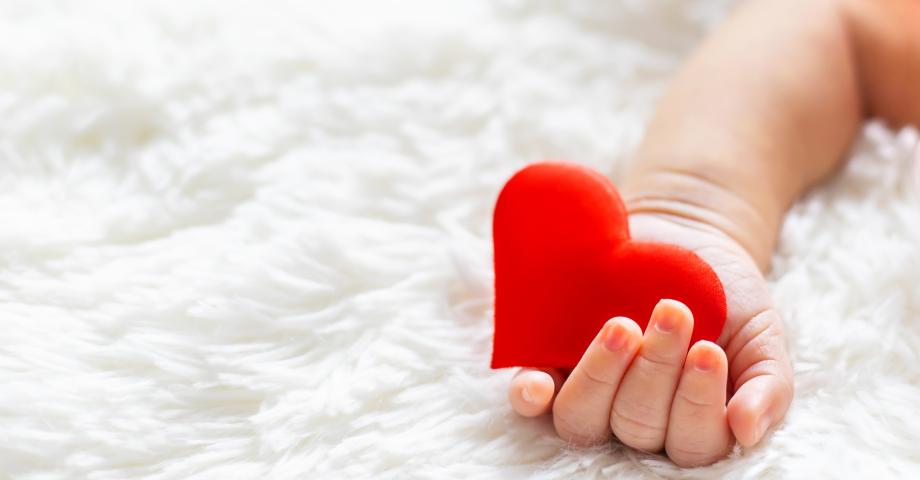 En bebis hand som håller ett dekorativt rött hjärta.