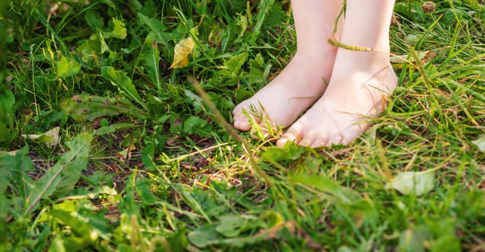 Flickan står barfota på en lång gräsmatta, bara hennes fötter syns.