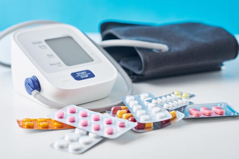 A digital blood pressure monitor and different medical pills on a white table.