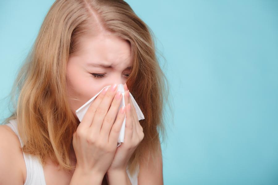 A sick girl sneezing in a tissue. 
