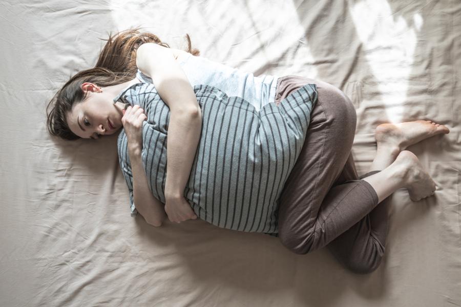 Young woman alone in the morning is lying in bed and hugging a pillow.